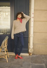 Lys beige strikket sweater med bølget kant, blå jeans og røde flade sko. Accessorieset med et rødt tørklæde og sat foran en blå dør.