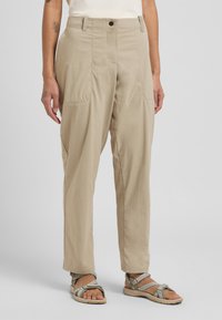 Pantaloni leggeri beige con una vestibilità ampia, dotati di tasche anteriori e una texture liscia, abbinati a sandali aperti.
