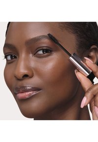 Máscara de pestañas negra con un cepillo en espiral en un tubo metálico elegante de color oro rosado. La modelo tiene la piel suave y radiante y un color de labios neutro.