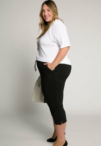 Witte kortärmige shirt gecombineerd met zwarte cropped broek met zijsplitten. De outfit heeft een relaxte pasvorm met zakken en een casual uitstraling.