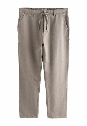 Detail osoby nosiacej béžové ľanové nohavice so zaväzovaným pásom a opaskovými slučkami, v kombinácii s bielou košeľou.