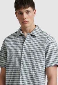 Korte mouwen shirt in wit en marineblauw ruitpatroon, gestructureerde stof, knoopsluiting, enkele borstzak.