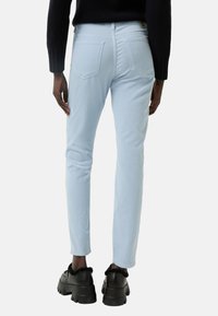 Světle modré džíny s úzkým střihem, se zadními kapsami a poutky na opasek. V par úzu s černými botami se silnou podrážkou. Textura vypadá hladce.