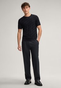 Maglietta nera a maniche corte in maglia con motivo testurizzato e scollo rotondo, abbinata a pantaloni grigio scuro e scarpe nere. Design semplice e moderno.