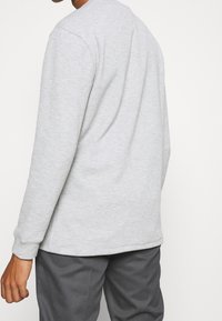 Grauer Langarm-Sweatshirt, hergestellt aus weichem Baumwollmix, mit rundem Halsauschnitt und gerippten Bündchen. Glatte Textur und lässiger Schnitt.