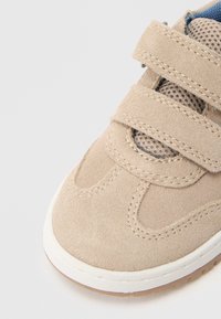 Beige semsket skinnsko med nettingpaneler, to borrelåsstropper, rund tå og hvit gummisåle med teksturerte grep.