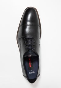 Chaussure de ville en cuir noir avec un bout arrondi, une tige lisse et un laçage. Présente un côté texturé et une semelle contrastante en marron.
