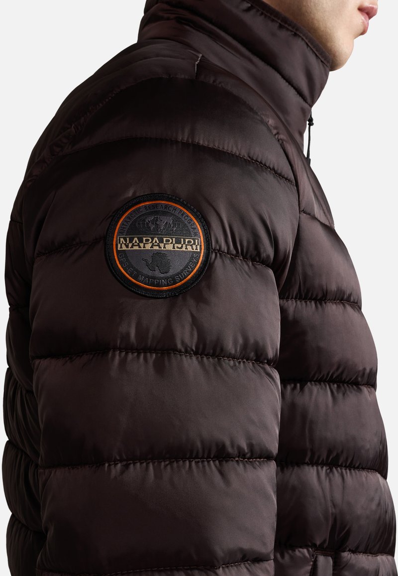 Braune Pufferjacke mit hohem Kragen, gestepptem Design und einem runden Logo-Patch am Oberarm. Glatte, glänzende Stoffoberfläche.