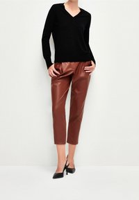 Svart v-ringad tröja i kombination med högmidjade, korta bruna byxor i konstläder och svarta spetsiga klackskor. Enkel, elegant silhuett.