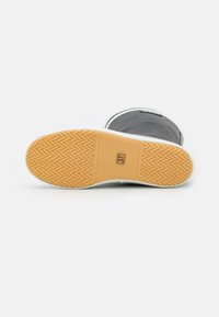 Musta kumisaapas, jossa on teksturoitu ruskea pohja, jossa on herringbone-kuvio. Koko etiketti "37" näkyvissä pohjan sivulla.