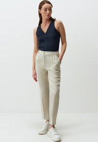 Body a costine blu navy con scollatura a V, abbinato a pantaloni beige con vita elasticizzata. Sneakers bianche completano l'outfit. Design minimalista, texture liscia.