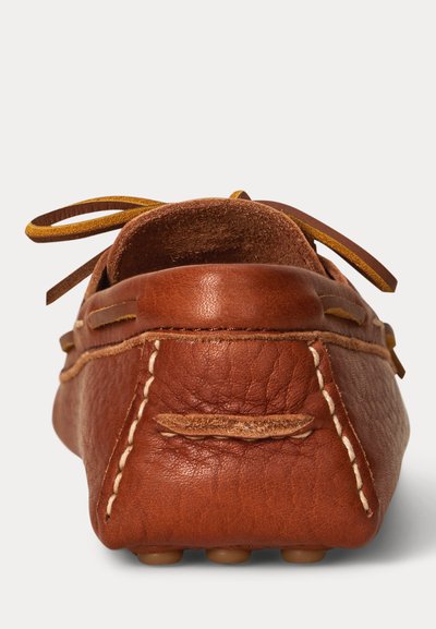 Mocassino in pelle marrone con cuciture visibili e un laccio in pelle annodato sul retro, visto dalla parte del tallone.