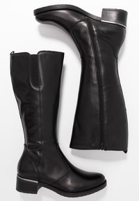 Par de botas altas de cuero negro con tacones bajos, cremallera lateral y panel elástico en la parte superior de la pantorrilla, mostradas sobre un fondo blanco.