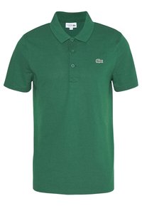 Grön kortärmad piké med tre knappar, ribbad krage och liten vit och grön krokodil-logotyp på vänster bröst.