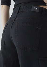 Svarte denimbukser med baklomme, elastisk midje og markerte sømmer. Merket "LTB" på baksiden.