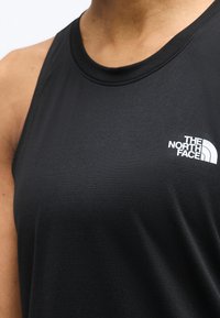 Κοντινό πλάνο ενός ατόμου που φοράει μαύρο αμάνικο τοπ με το λογότυπο The North Face στο πάνω δεξιό μέρος του στήθους.