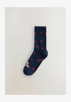 Marineblå sokker med røde hjerter og et mønstret brunt dyredesign. Blødt strikket materiale med standard crew-form og ribbet kant.