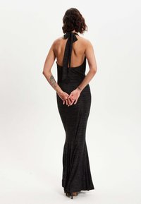 Black halter neck gown with an open back, fitted silhouette, and flared hem. Soft, textured fabric with a slight shimmer and ankle-length.