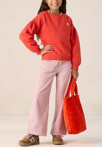 Pull en rouge avec des manches bouffantes et un logo en cœur, pantalon large rayé rose, baskets brunes à motifs léopard, et un sac à main matelassé orange.