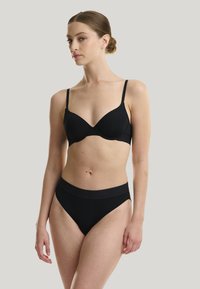Set di lingerie nera composto da un reggiseno con coppe preformate e lisce, dotato di spalline regolabili, e un perizoma a vita alta abbinato con un morbido elastico.