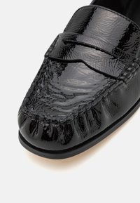 Zwarte gepatenteerde leren loafers met een textuurafwerking, voorzien van een gestikte neus, moccasinstijl bovenkant en vlakke rubberen zool.