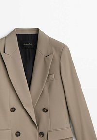 Beiger Doppelreiher-Blazer mit Spitzrevers, zwei Vorder Taschen und dunkelbraunen Knöpfen. Glatter Stoff mit maßgeschneidertem Design.