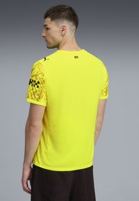 Kortärmad gul träningsskjorta med mönstrade ärmar. Har rund halsringning och logotypdetalj på baksidan. Materialet har en slät yta.