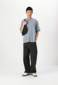 Camiseta de gran tamaño en azul claro, pantalones de mezclilla negros, zapatillas gris y blancas con rayas, y una pequeña bandolera negra.