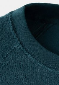 Close-up of a dark teal textured terry cloth sweatshirt neckline with ribbed collar and stitched seams.