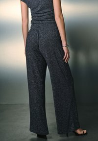 Zwarte, glinsterende wijde broekspijpen met een elastische tailleband, met een gladde textuur en vloeiend ontwerp, gecombineerd met sandalen met hoge hakken.