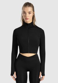 Veste athlétique noire courte avec un col haut, fermeture éclair intégrale et manches longues. Texture lisse, design ajusté et détail découpé à la taille.