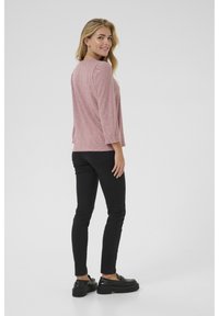 Rosa, strukturierte Bluse mit Lochmuster, 3/4-Ärmeln, kombiniert mit schwarzen Slim-Fit-Hosen und schwarzen Plateauschuhen.