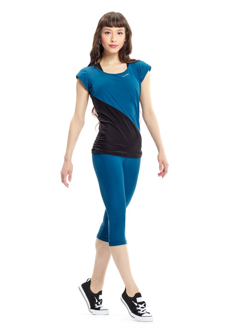 Teal and black athletic top with short sleeves, curved design; paired with teal capri leggings, finished with black sneakers.