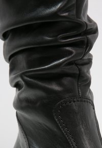 Czarne skórzane buty z luźnym fasonem, charakteryzujące się błyszczącą teksturą i widocznymi detalami szycia wzdłuż boku.