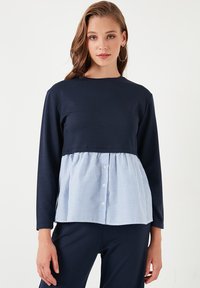 Top a maniche lunghe navy con un orlo a peplum a righe bianche e blu, arricchito da dettagli con bottoni, che unisce tessuti lisci e testurizzati.