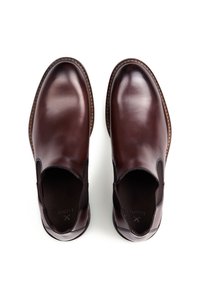 Zapatos de cuero marrón tipo slip-on con paneles elásticos en los costados, punta redondeada y costura contrastante en la suela. Acabado liso y pulido.