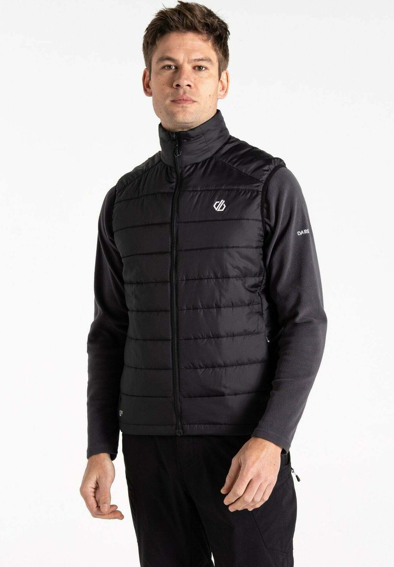 Black padded vest with high collar, zip closure, and logo on chest; worn over a black long-sleeve shirt, set against a white background.