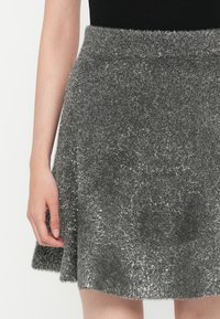 Siva puhasta krila z bleščečo teksturo in razširjeno zasnovo, s visokim pasom in robom, ki se konča tik nad kolenom.