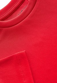 Camiseta roja texturizada con cuello redondo y un bolsillo en el lado izquierdo, con detalles de costura visibles.