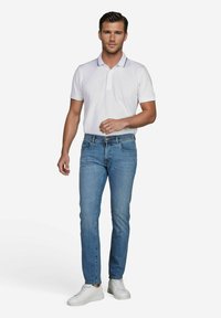 Witte polo met kraag, slim-fit blauwe jeans en witte sneakers. Opvallende details zijn schouderstrepen en een aansluitend ontwerp.