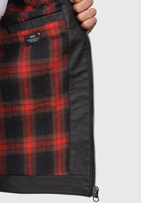 Das Innere der schwarzen Lederjacke verfügt über ein rot-schwarz kariertes Futter mit einer Tasche und einem Markenetikett. Reißverschlussdetails am Rand.
