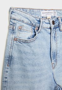 Helle blaue Jeans mit hoher Taille, fünf Taschen, Hardware in Kupferoptik und dezentem Ausbleichen, mit einem Etikett am Bund.