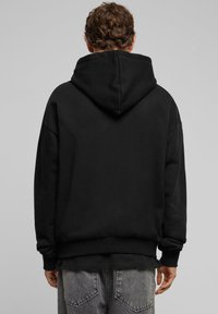 Zwarte hoodie met een ruime snit, voorzien van een grote capuchon, geribbelde manchetten en een zoom. Zacht stoffen met minimale details, gedragen met vervaagde grijze jeans.