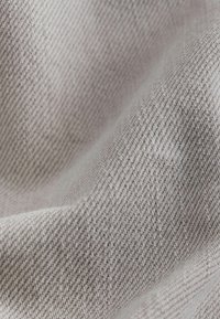 Gros plan sur un tissu texturé gris clair avec un motif tissé diagonal et des plis subtils créant de douces ombres.