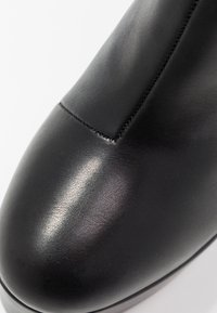Botín negro que presenta un acabado de cuero suave, punta redondeada y un detalle de costura minimalista a lo largo de las costuras.