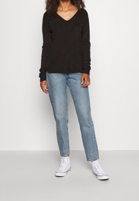 Svart stickad tröja med V-ringning, kombinerad med ljusblå raka jeans och vita högknäade sneakers. Enkel design, ribbade ärmslut.