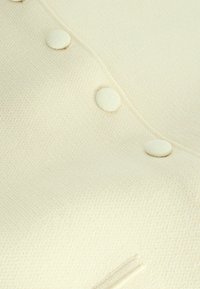 Tissu en maille couleur crème avec une texture douce, doté de trois boutons structurés et d'un motif côtelé subtil le long de la couture.