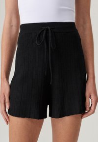 Svarta stickade shorts med en texturerad ribbad mönster, elastisk midja och dragsko. Har en lätt scalloped nederkant.