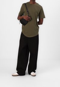 Camiseta de manga corta color verde oliva con dobladillo curvado, combinada con pantalones holgados negros y un pequeño bolso bandolera negro con una correa de marca.