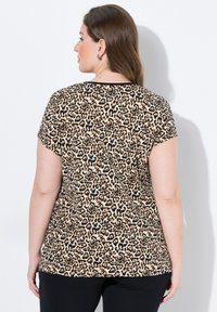 Krátký rukáv top s leopardím potiskem v béžové a černé barvě, s kulatým výstřihem. Hladká textura s volným střihem, doplněný černými kalhotami.